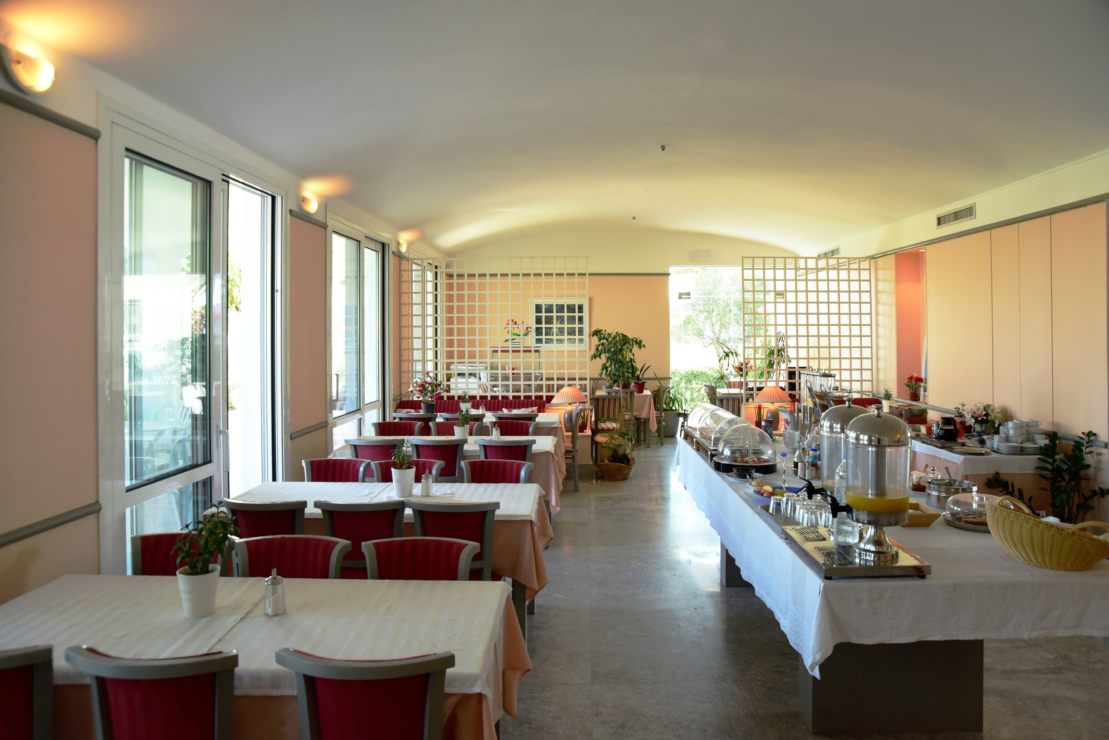 A spacious dining area with multiple tables and chairs, large windows, and a buffet setup.