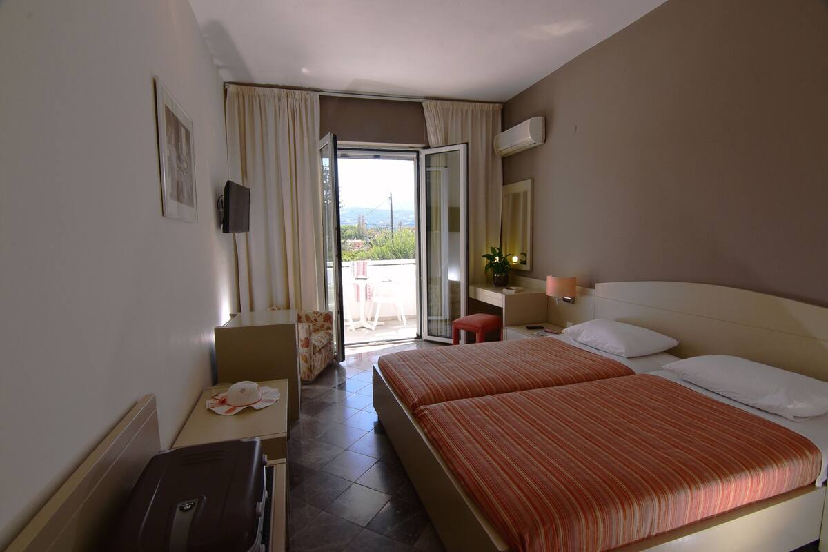 A hotel room with two beds, a desk, a chair, a suitcase, and a sliding glass door leading to an outdoor area.