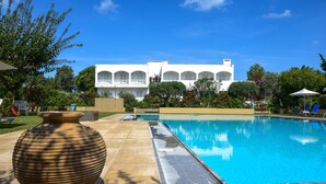 A swimming pool with a white building in the background, surrounded by greenery. - Mantenia Hotel (Rethymno)