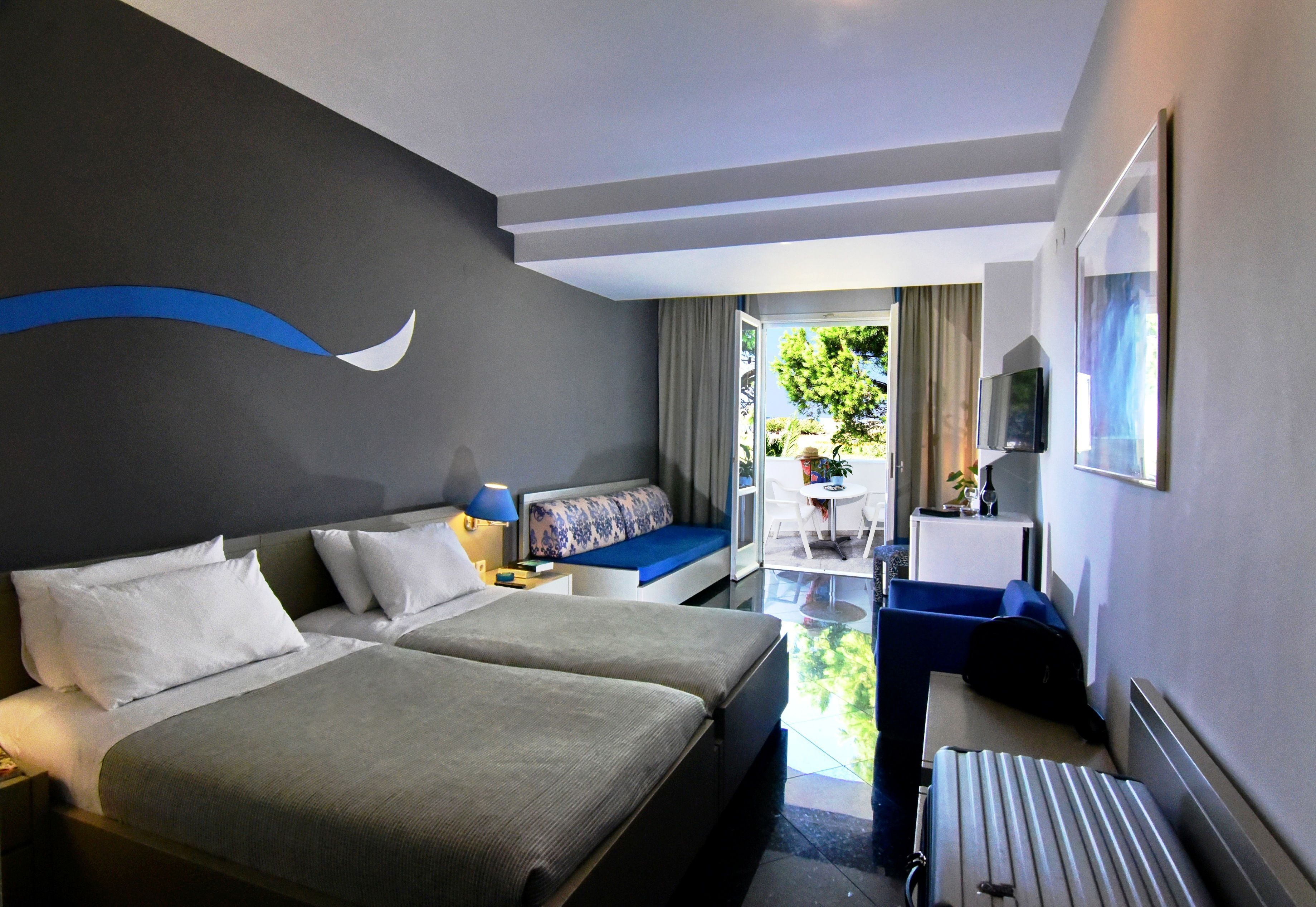 A hotel room with two beds, a desk, a chair, a TV, and a view of the outdoors.