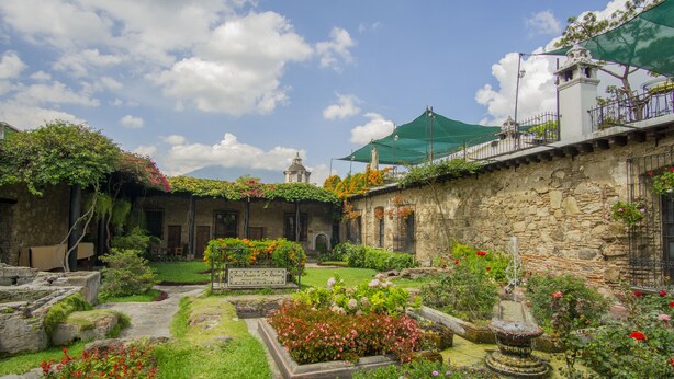 A courtyard with stone walls, a fountain, and various plants and flowers. - Hotel Posada de Don Rodrigo Antigua (Antigua Guatemala)