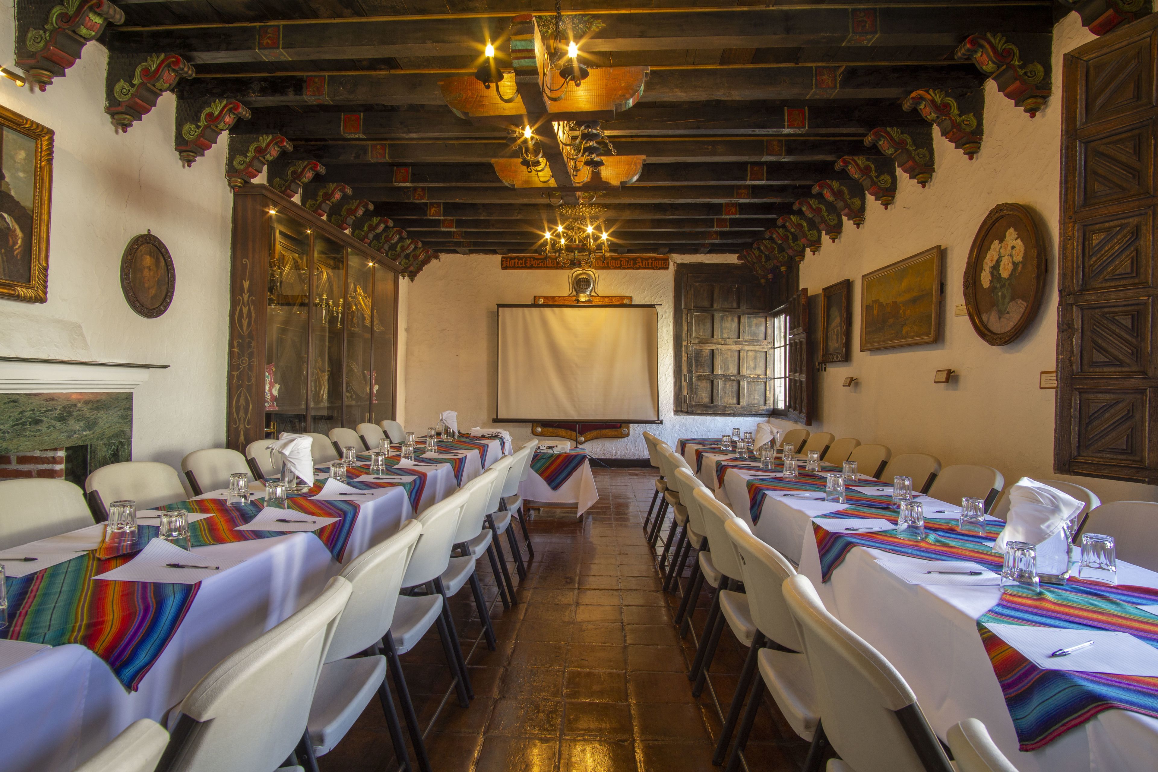 Un salón de conferencias con mesas largas, sillas blancas y techo de madera.