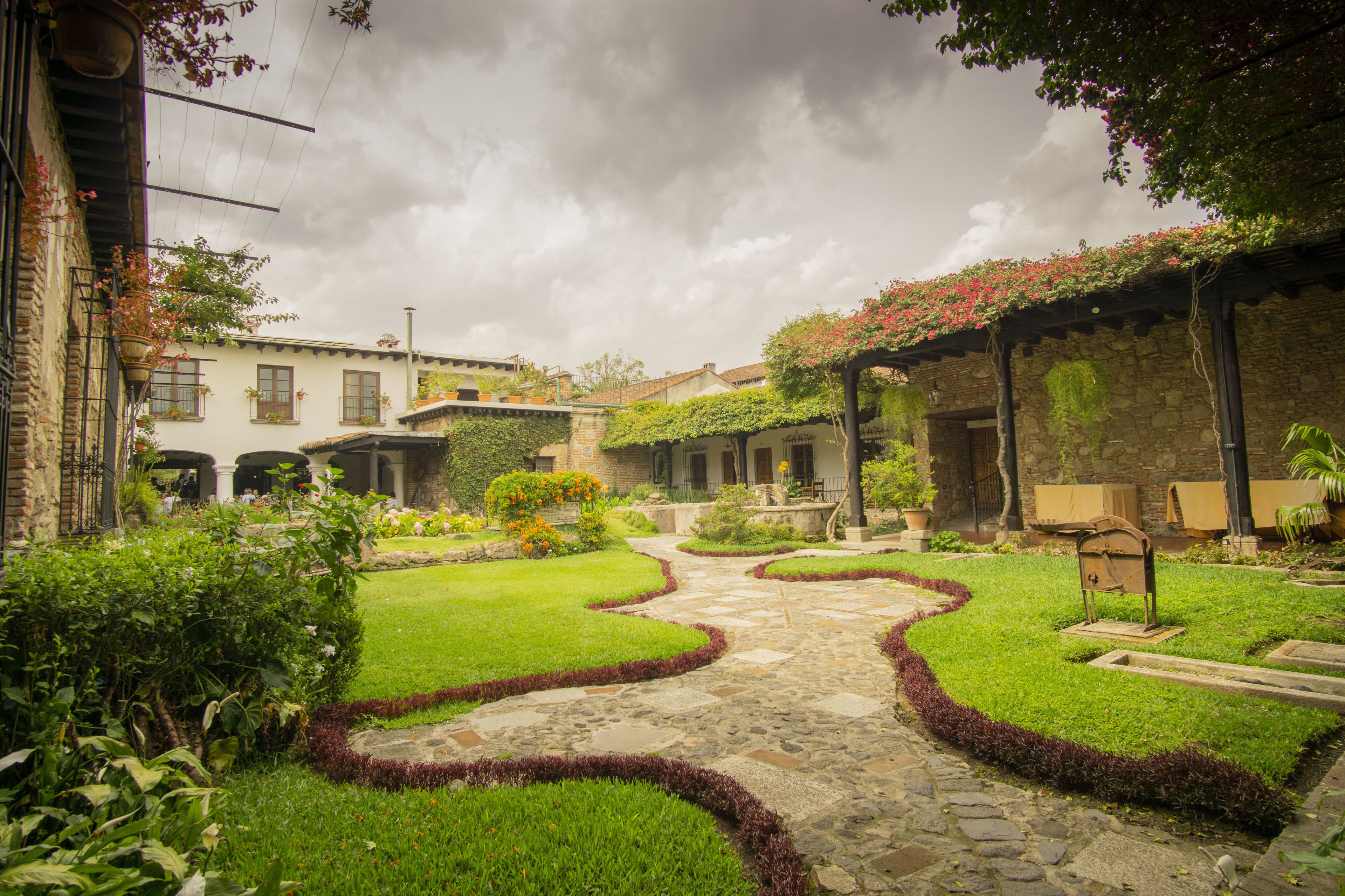 Um pátio com caminho de pedra, gramados verdes e uma pérgola coberta de flores.