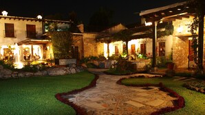 A well-lit courtyard with a stone pathway, surrounded by manicured lawns and a stone wall. - Hotel Posada de Don Rodrigo Antigua (Antigua Guatemala)
