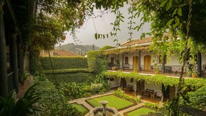 A courtyard with a fountain, neatly trimmed hedges, and a building with arched windows and a tiled roof. - Hotel Posada de Don Rodrigo Antigua (Antigua Guatemala)