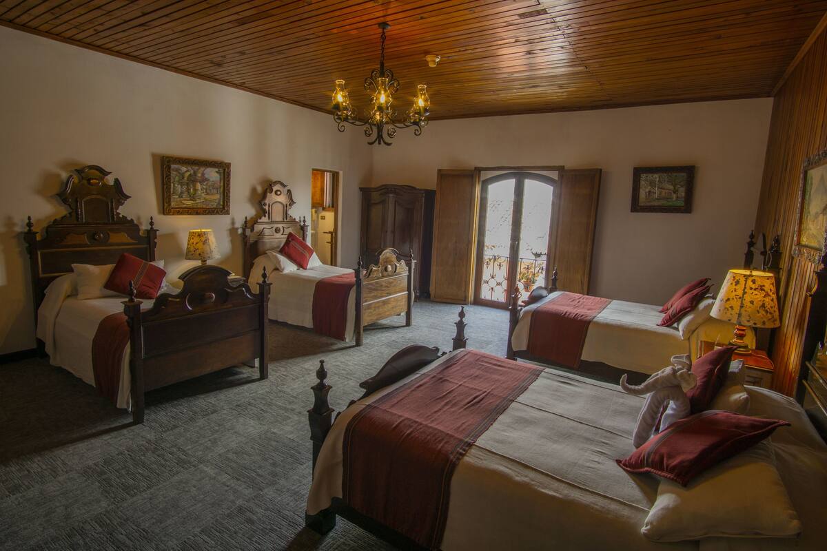 A hotel room with two beds, wooden furniture, a chandelier, and a view of the outside.