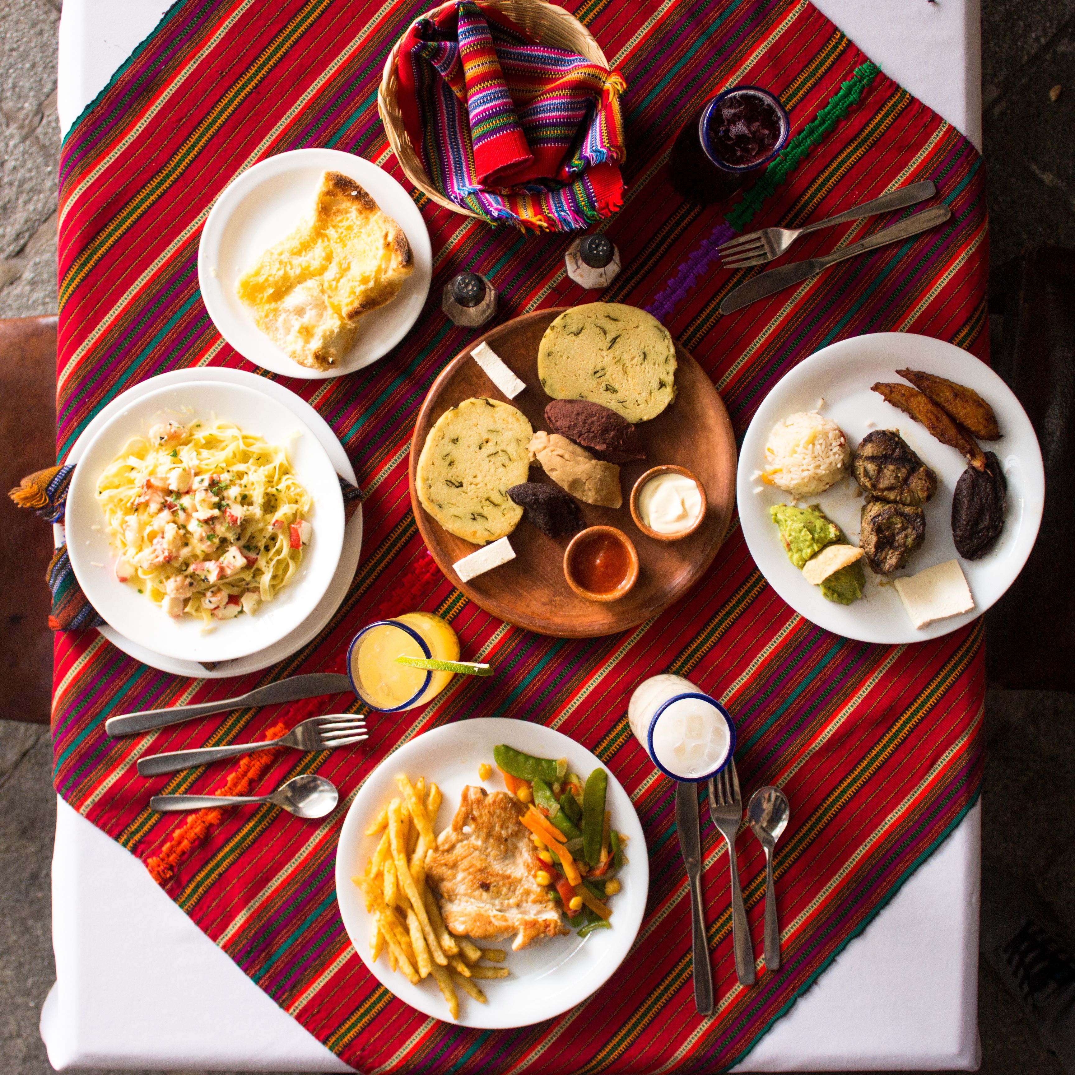 Una mesa servida con diversos platos, incluyendo pan, arroz y verduras, sobre un mantel tejido y colorido.