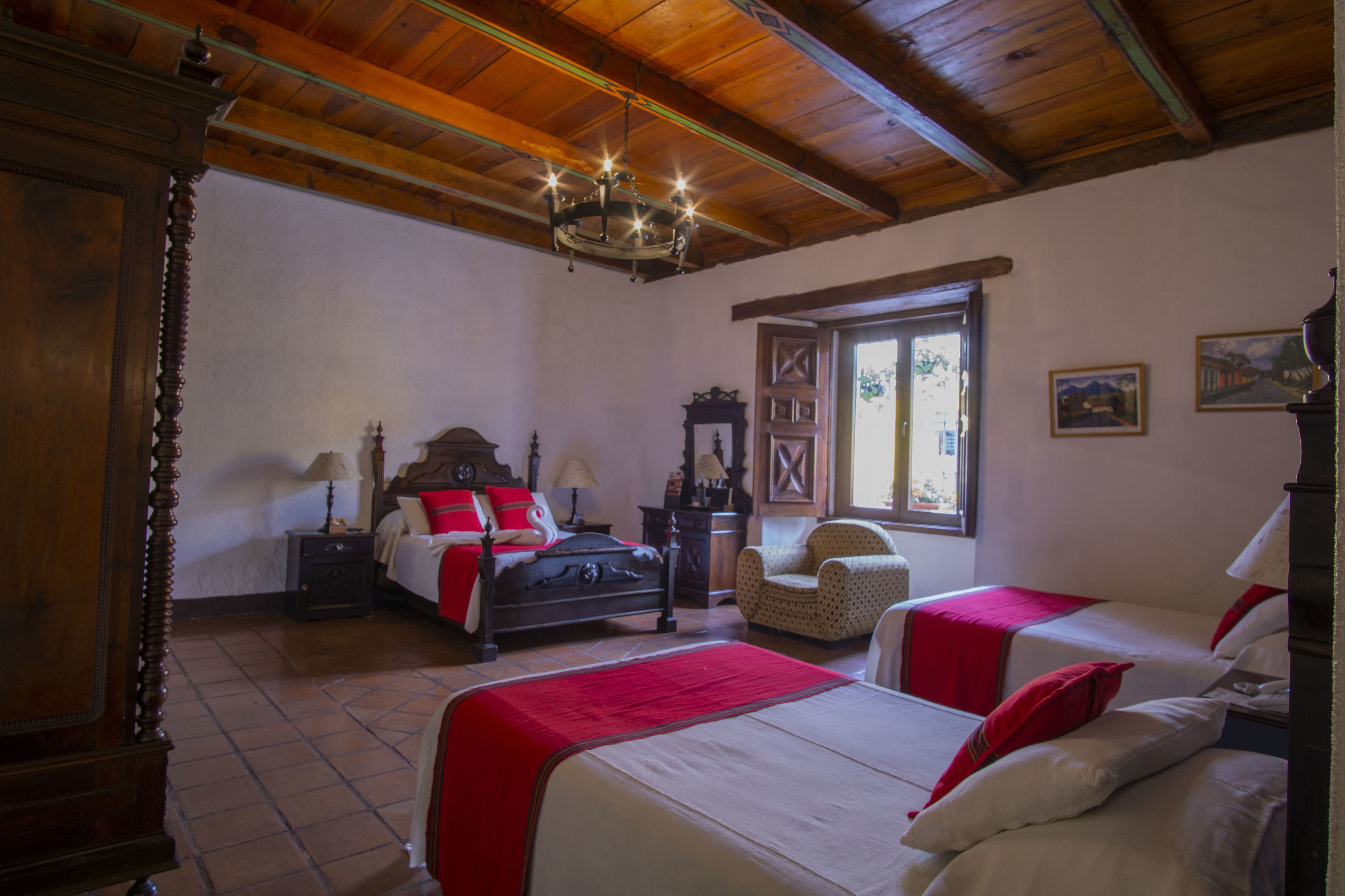 A bedroom with two beds, a wooden ceiling, a chandelier, a chair, and a window with a view.