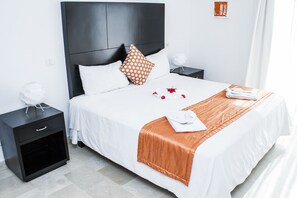 A neatly made bed with white and orange bedding, a black headboard, and a small bedside table with a lamp.