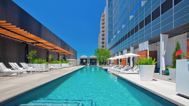 A swimming pool with lounge chairs and umbrellas, surrounded by modern buildings. - W Austin (Austin)