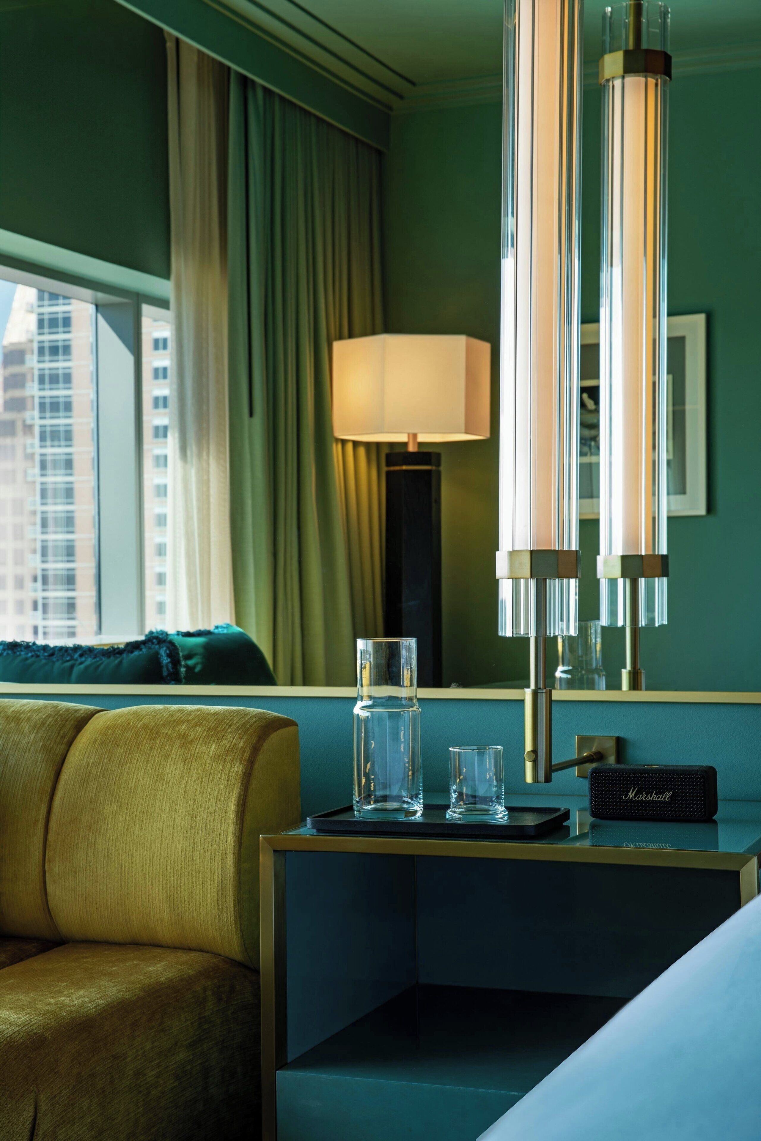 A hotel room with a bed, a nightstand with a lamp, a glass of water, and a Marshall speaker.