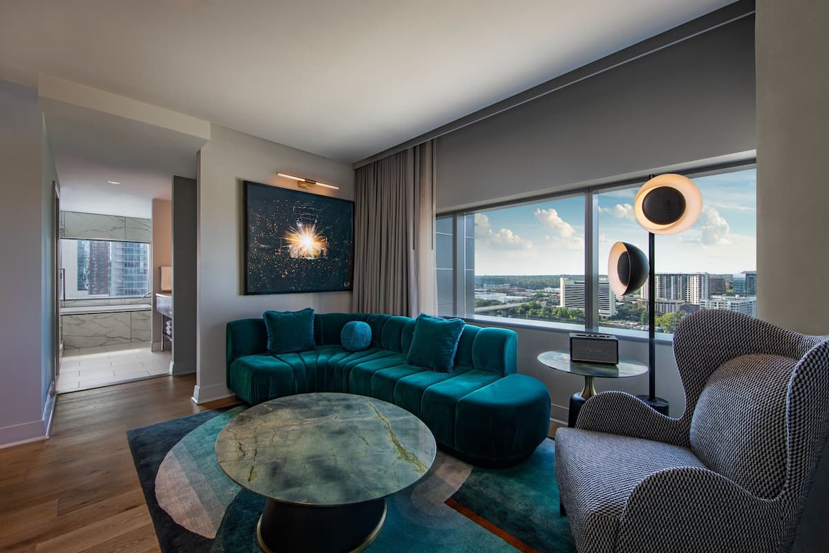 A modern living room with a teal sectional sofa, a round coffee table, and a city view through large windows.
