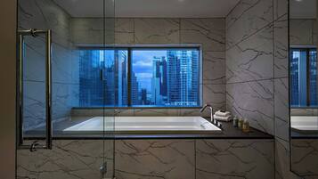 Un baño moderno con una bañera grande, una ducha con mampara de vidrio y vistas a la ciudad a través de un ventanal.
