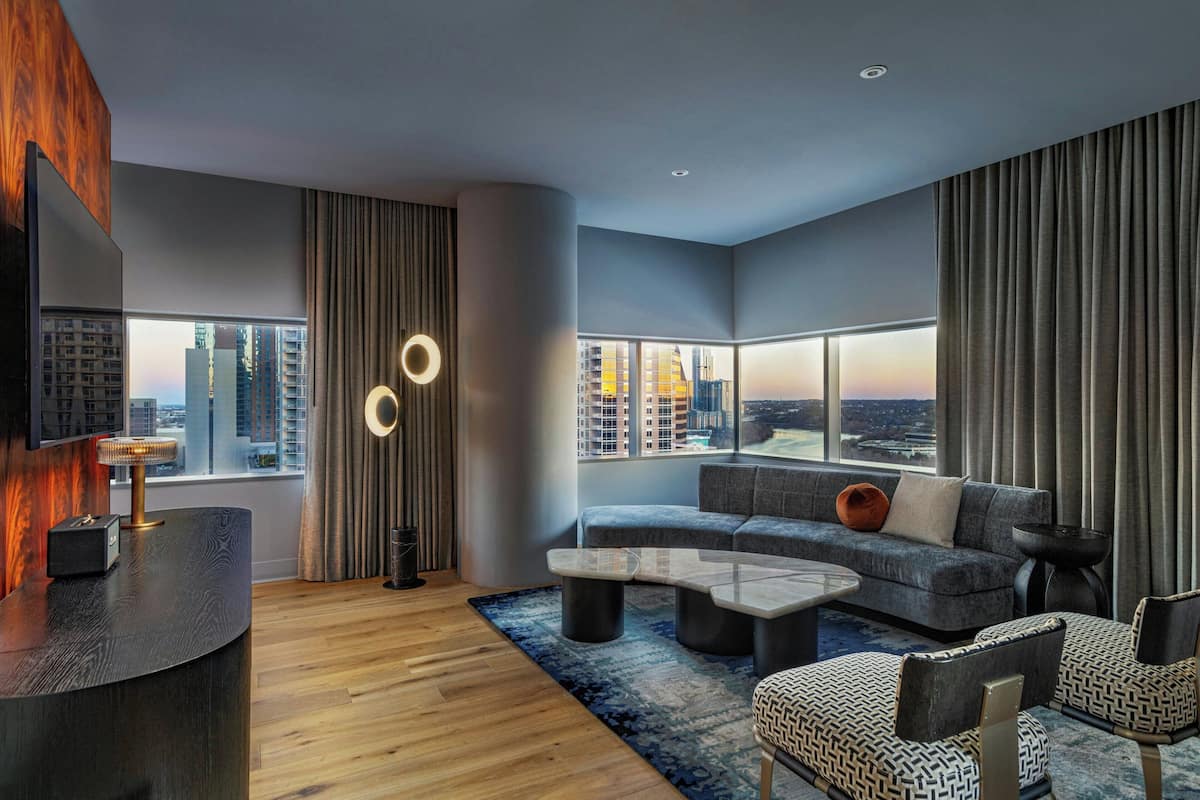 A modern living room with a curved reception desk, a sectional sofa, and a large window offering a city view.