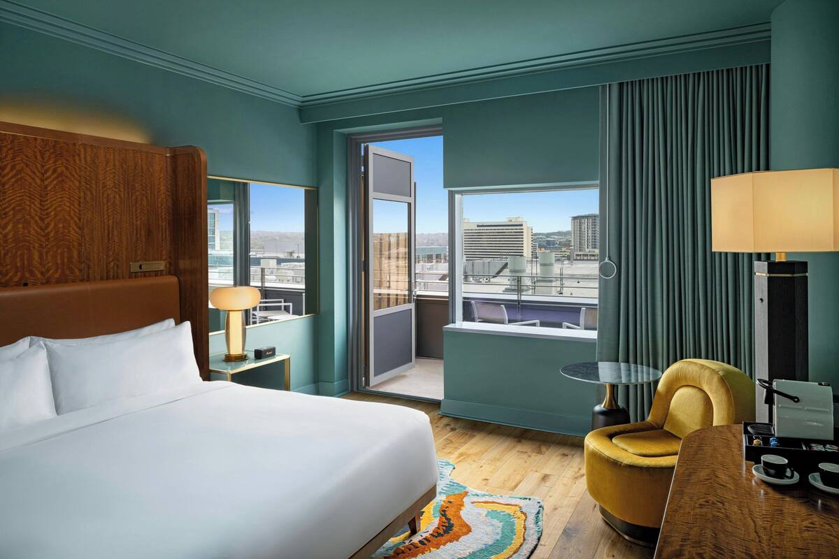 A hotel room with a bed, a desk, a chair, a table, and a view of the city.