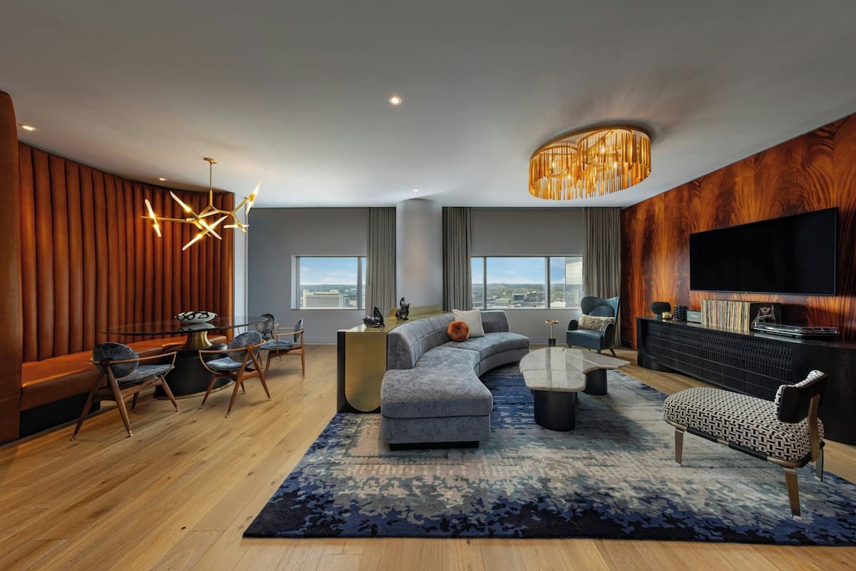 A modern living room with a sectional sofa, a coffee table, and a TV. There is a wooden accent wall and a large window providing a view.