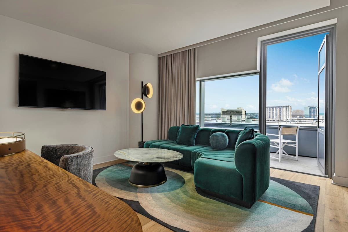 A modern living room with a green sofa, a round coffee table, and a flat-screen TV mounted on the wall.