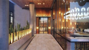 A modern restaurant entrance with a sign, a glass wall with interior lighting, and a cactus display. - W Austin (Austin)