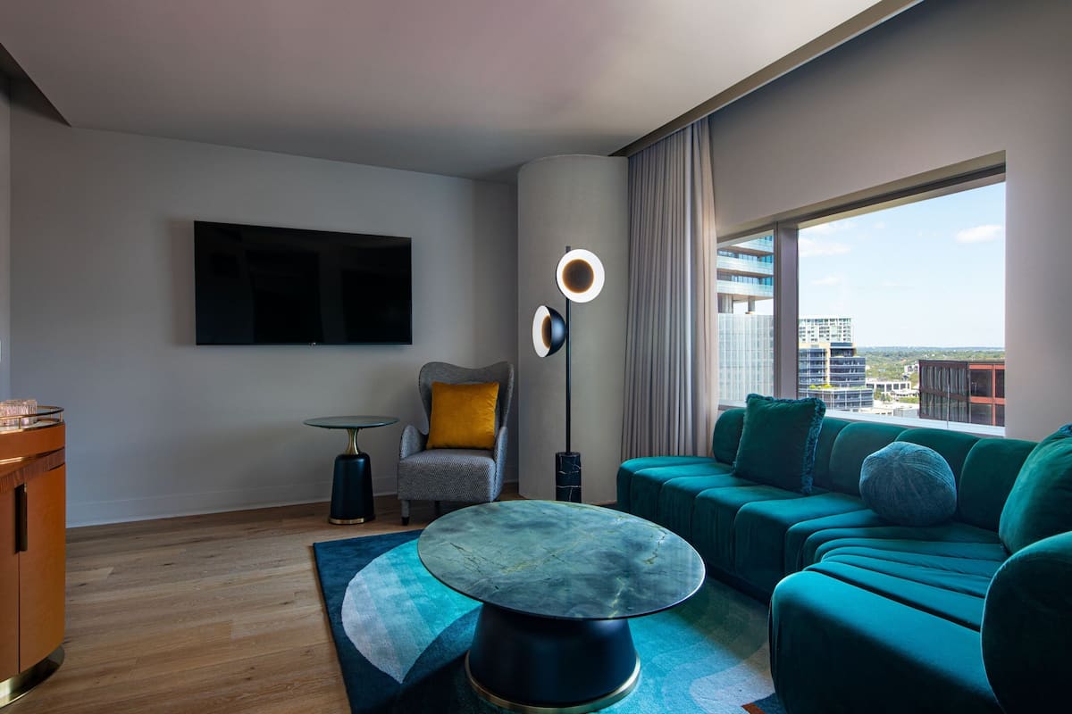 A modern living room with a flat-screen TV, a round coffee table, a sofa, and a view of the cityscape through large windows.