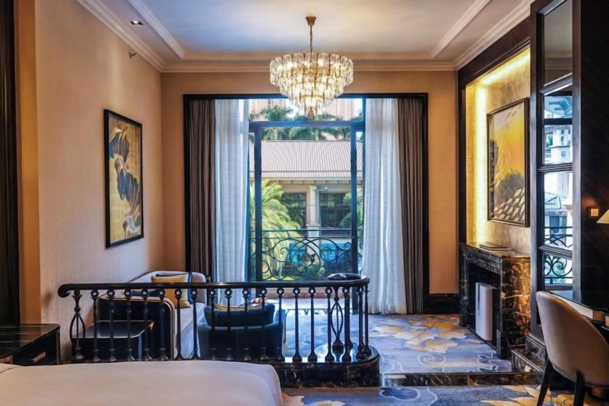 Une chambre d’hôtel avec un lit, un lustre, un balcon avec vue et une cheminée.