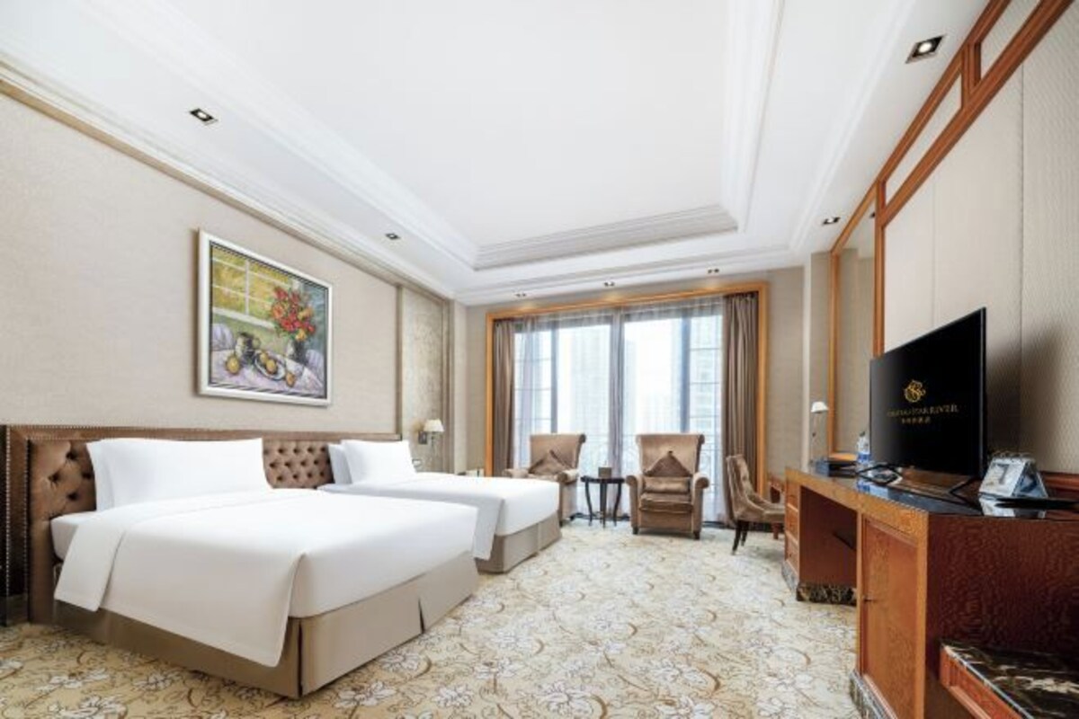 Une chambre d’hôtel avec deux lits, une télévision, un bureau et une fenêtre avec des rideaux.