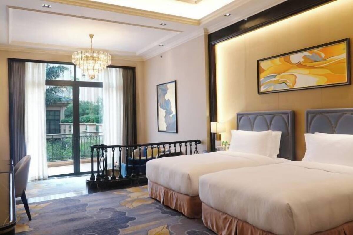 Ein Hotelzimmer mit zwei Betten, einem Balkon, einer Chandelüster und einem Gemälde an der Wand.