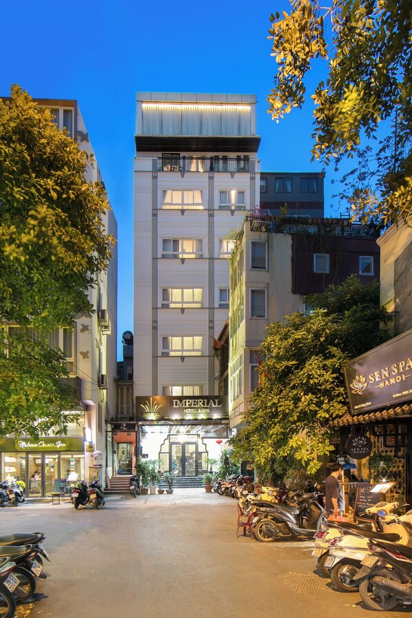 A hotel with a modern facade, a visible entrance, and a row of parked scooters. - Imperial Hotel & Spa (Hanoi)
