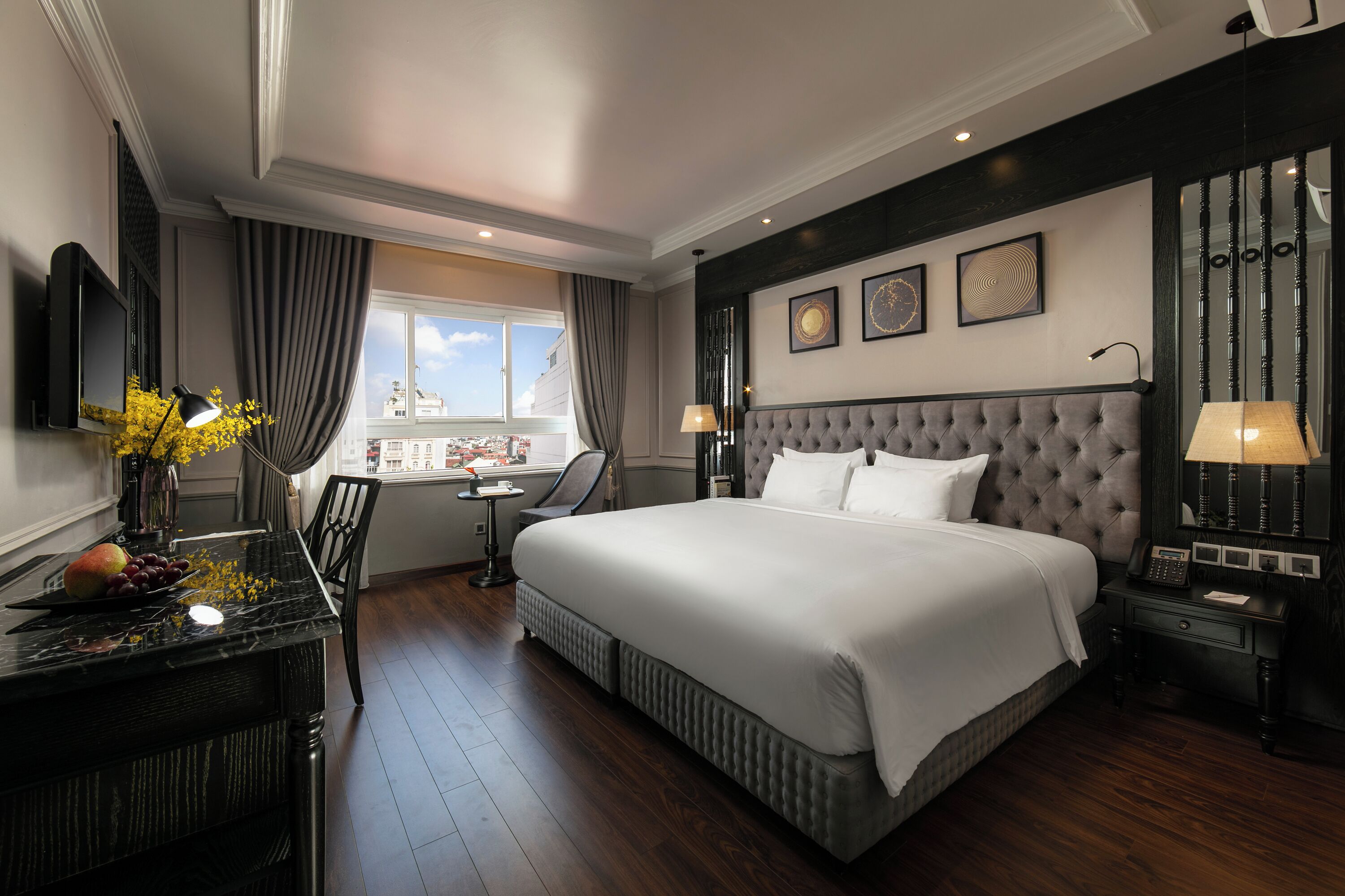 A hotel room with a large bed, a desk with a lamp, a chair, and a view of the city.