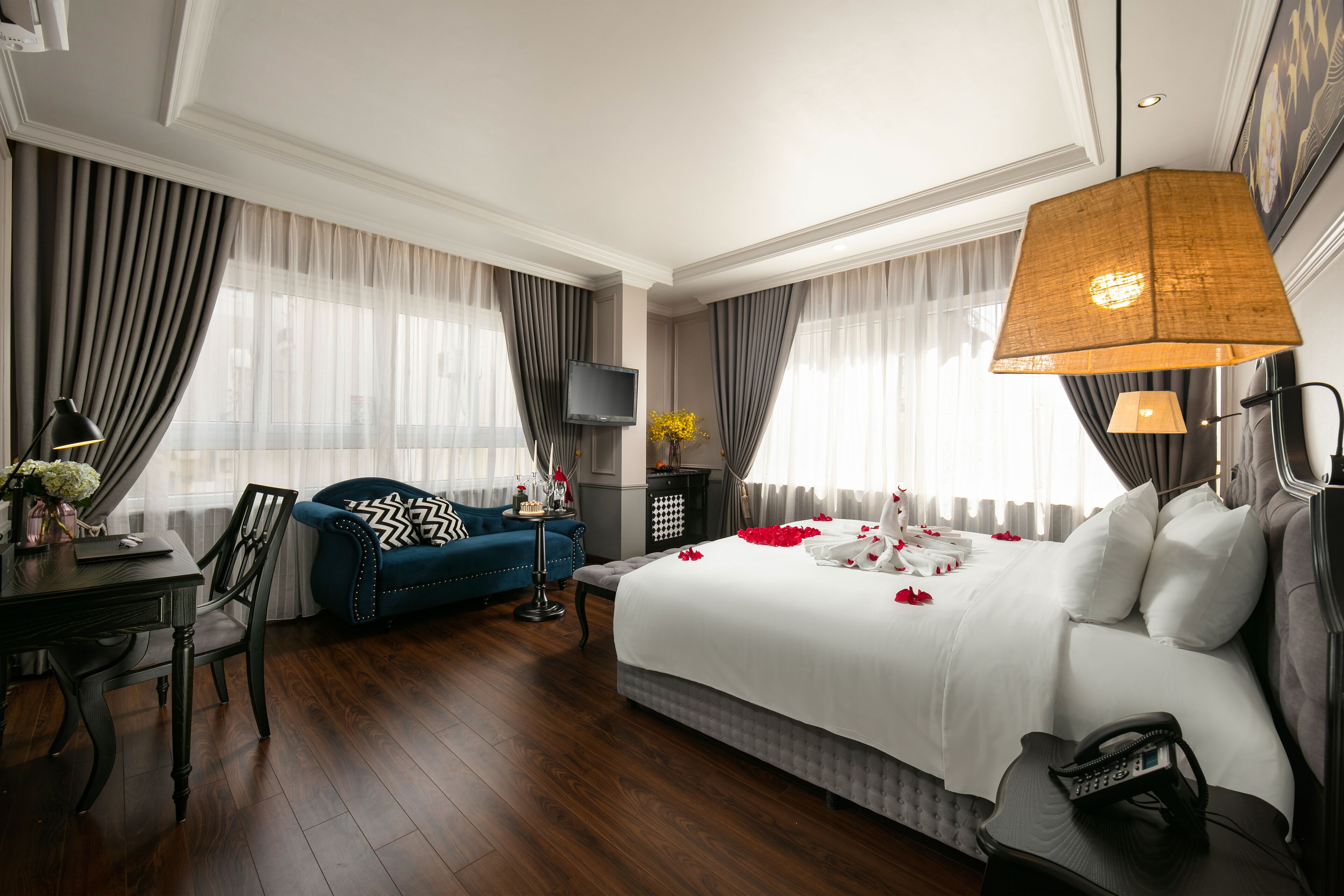 Habitació d'hotel amb un llit gran, una taula de treball amb una cadira, un sofà blau i una televisió.