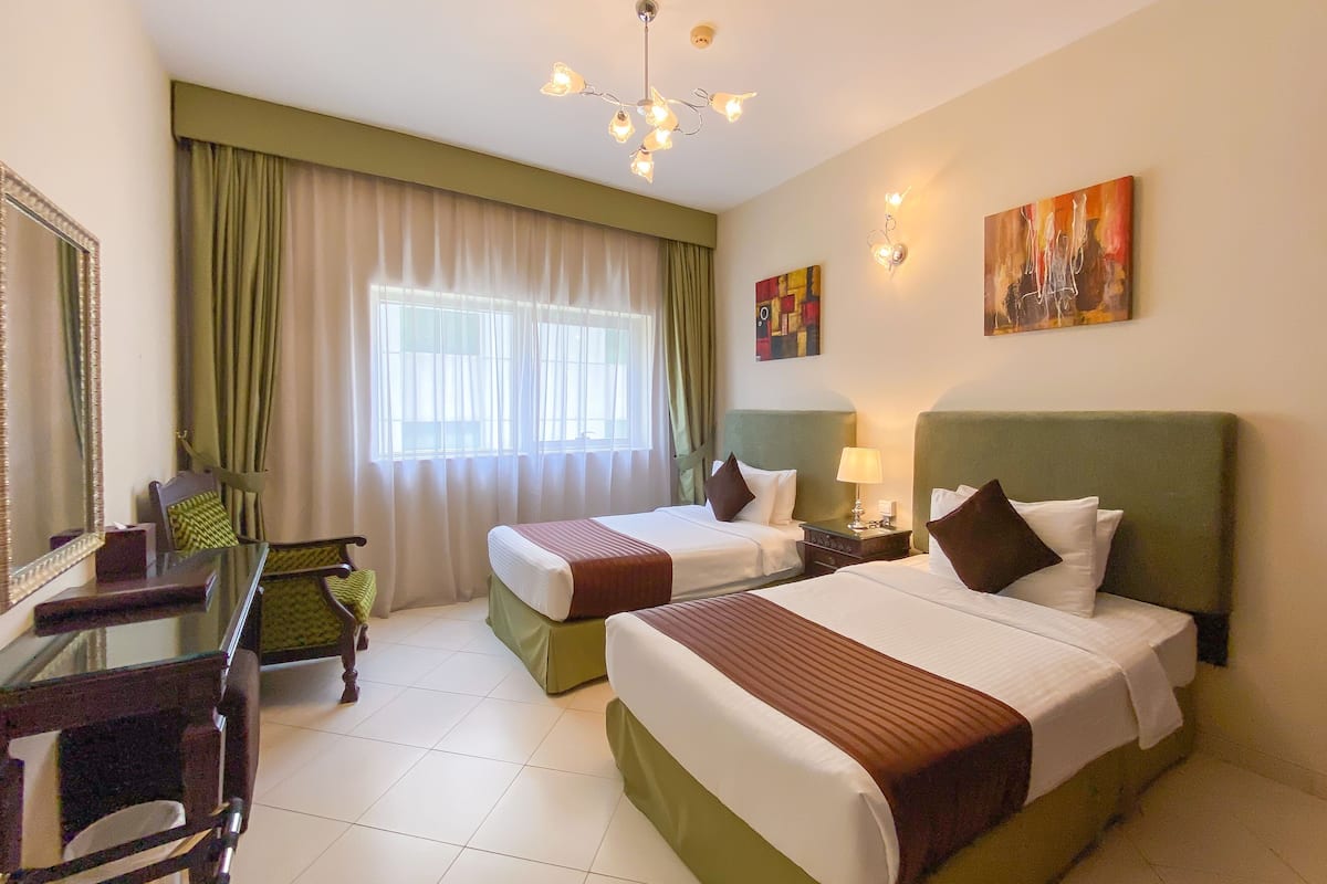 A hotel room with two beds, a desk, a chair, and a large window with curtains.