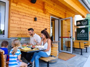 A family dining at an outdoor table with a wooden exterior and a sign for Albergo Dimaro.