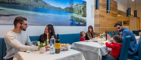 Ein Restaurant mit gedeckten Tischen, einem großen Landschaftsbild von Bergen an der Wand und moderner Pendelleuchten.