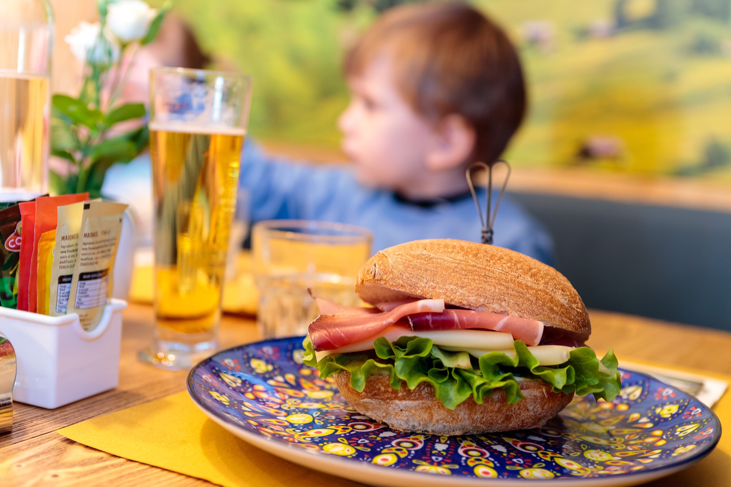 A sandwich on a plate with a beer glass and condiments in the background.
