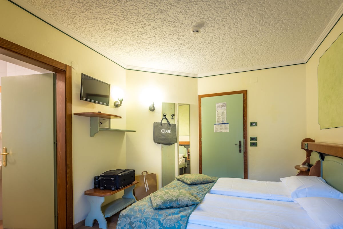 A hotel room with a bed, a desk, a chair, a television, and a door.