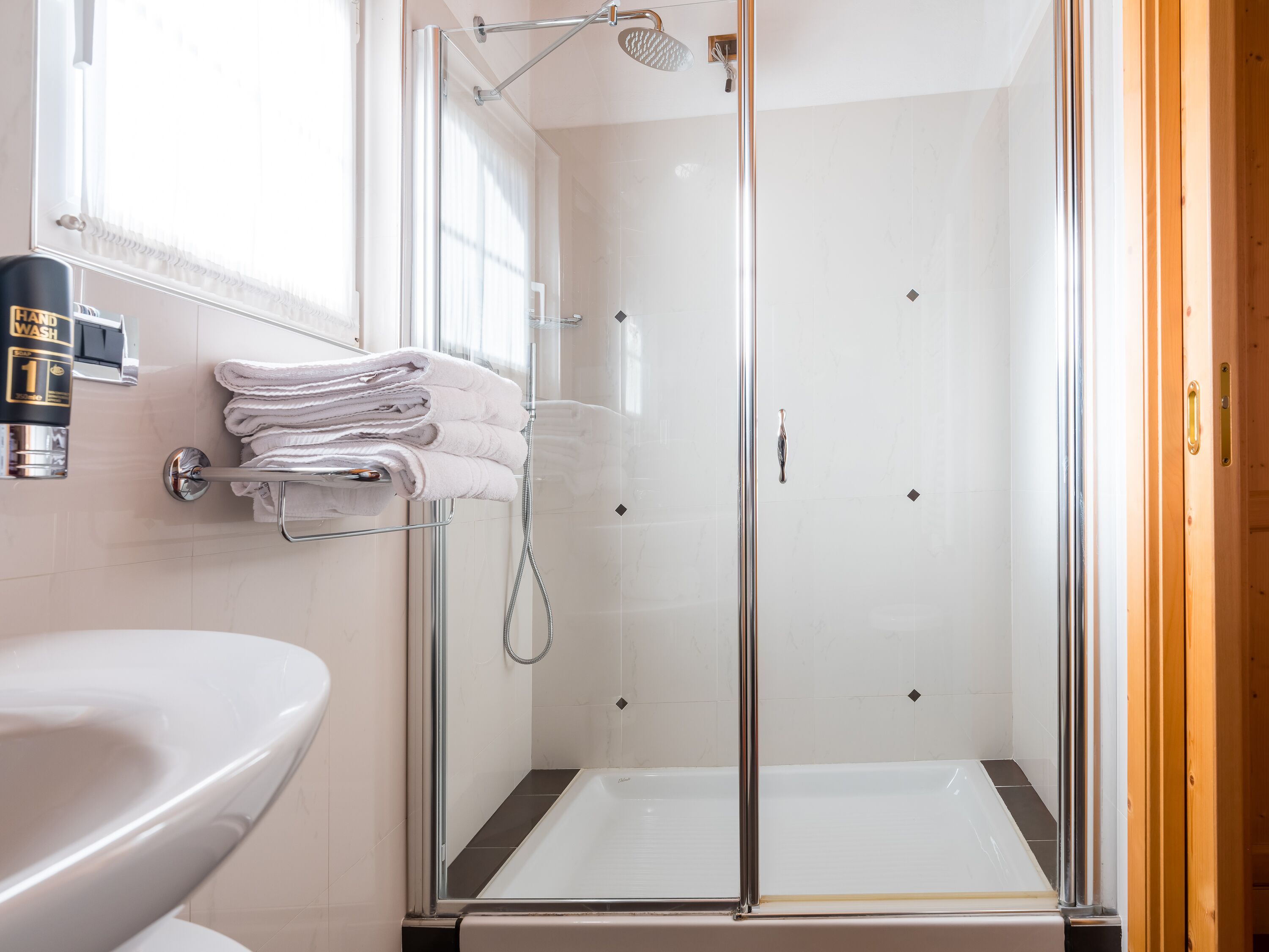 Un baño moderno con ducha de mampara de vidrio, un lavamanos y un perchero para toallas.