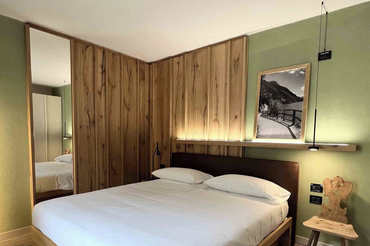 A modern bedroom with a wooden bed frame, a large mirror, and a mounted picture.
