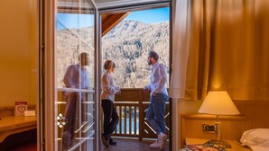 A hotel room with a wooden balcony, a red carpet, a wooden nightstand with a lamp, and a bed with white linens. - Albergo Dimaro Wellness & Family Hotel (Dimaro Folgarida)