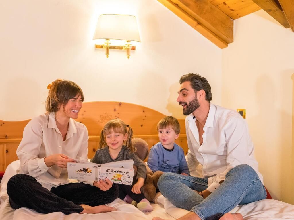 Una famiglia seduta su un letto in una stanza con testiera in legno e lampada a parete.