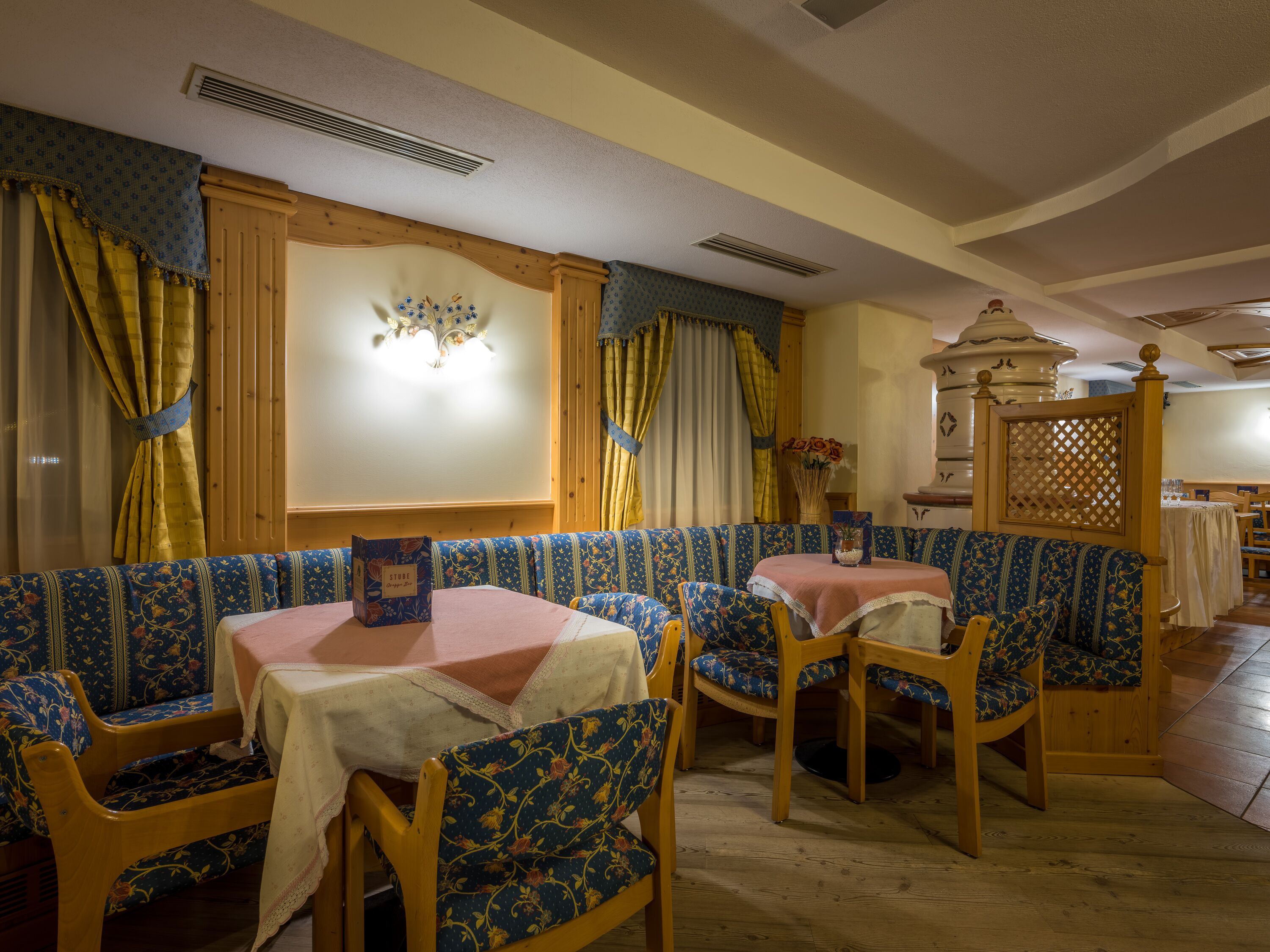 A cozy dining area with patterned blue and yellow upholstered booths, wooden chairs, and a table with a pink tablecloth.