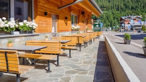 A wooden building with outdoor seating and a stone floor. - Albergo Dimaro Wellness & Family Hotel (Dimaro Folgarida)