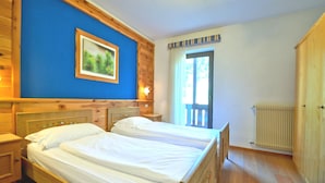 Een kamer met twee bedden, houten wanden, een groot raam en een radiator.