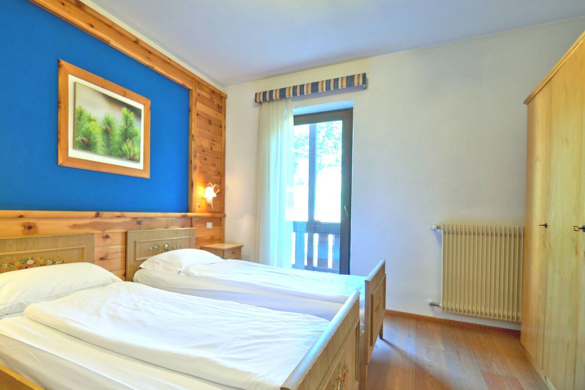 A room with two beds, wooden walls, a large window, and a radiator.