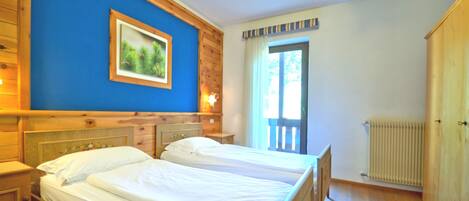 A room with two beds, wooden walls, a large window, and a radiator.