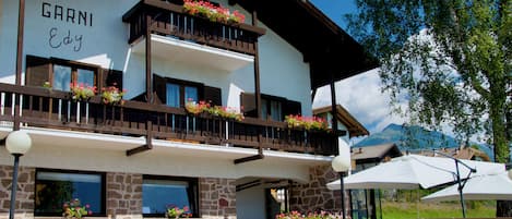 Um edifício chamado GARNI Edy com varandas decoradas com flores, paredes de pedra e área de estar ao ar livre.