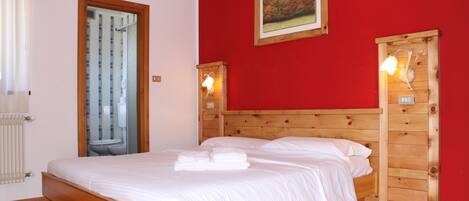 Un dormitorio con cama de madera, paredes rojas y una ventana con cortinas.