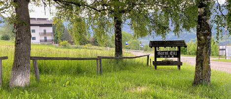 A signpost with the name 'Karni Gj' in a grassy area with trees and a building in the background.