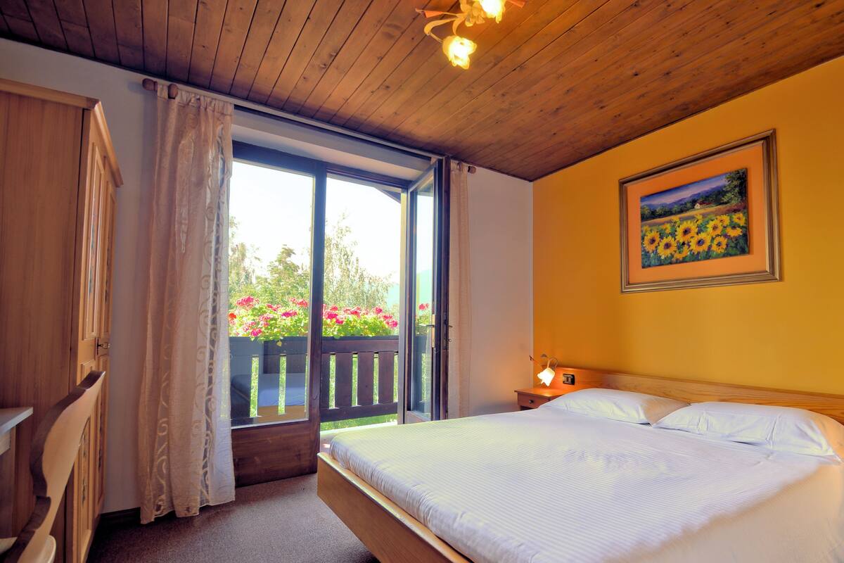 A bedroom with a bed, a nightstand, a painting, and a view of a garden through a sliding door.