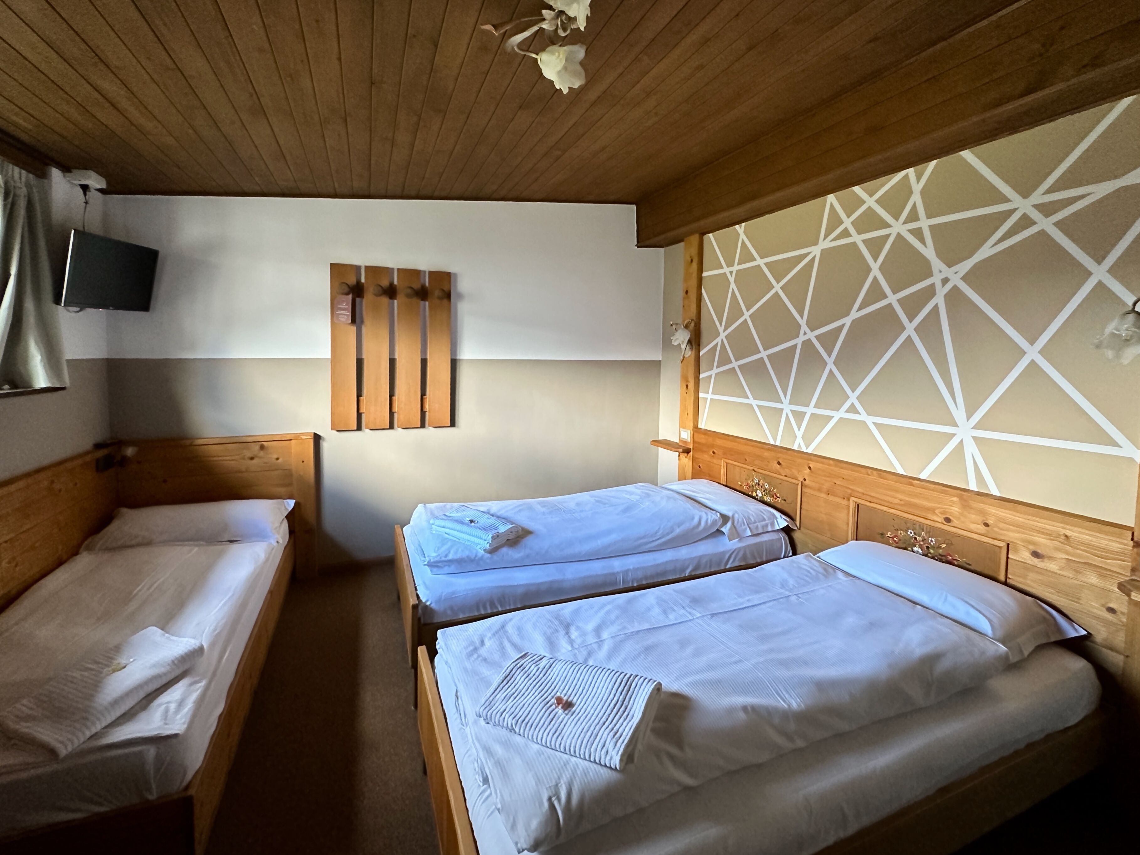 Una habitación con dos camas de madera, un televisor montado y una pared con un diseño geométrico.