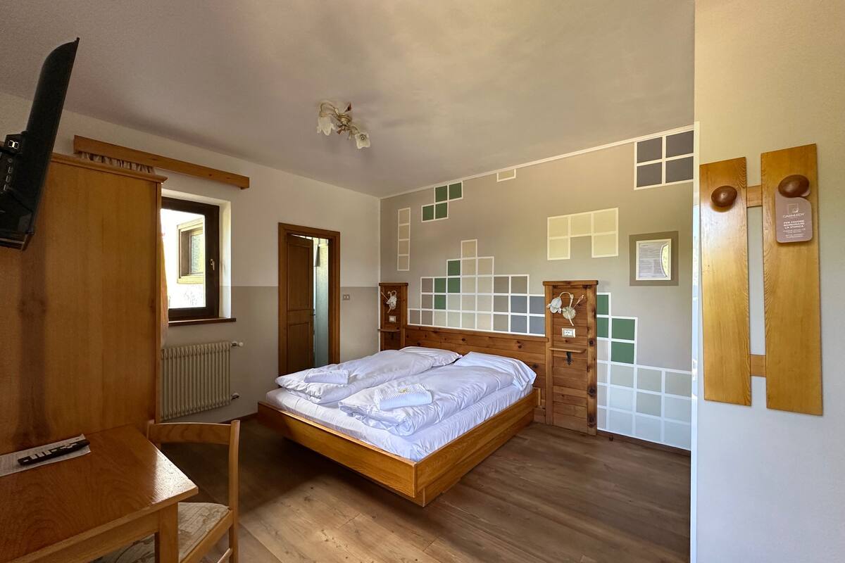 A bedroom with a wooden bed, a desk, and a chair. There is a window and a radiator.