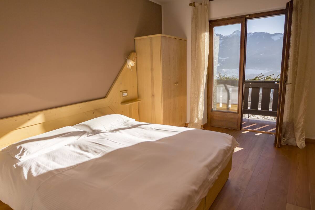 A bedroom with a wooden headboard, a bed with white linens, a nightstand, and a view of mountains through a sliding glass door.